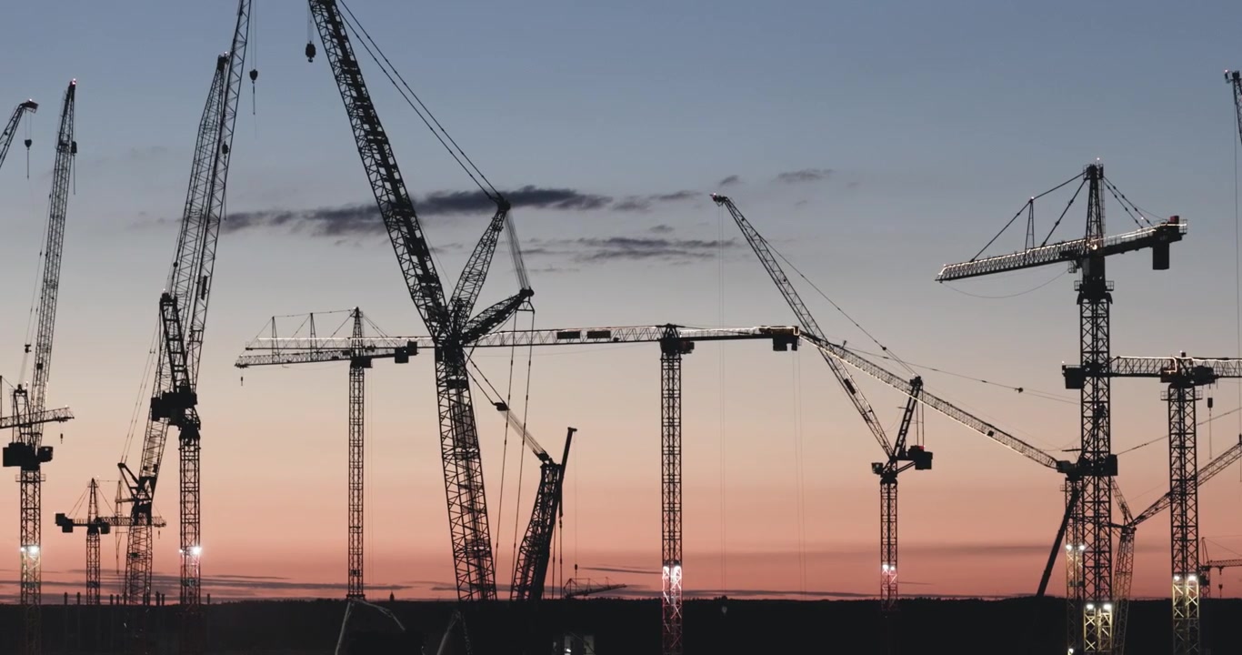 Numerous industrial tower cranes working on a massive semiconductor plant construction site during sunset in Saxony, Germany