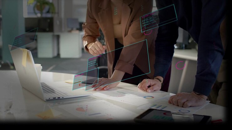 Woman pointing laptop using pad, man marking business charts, activating AR panels analyzing graphs