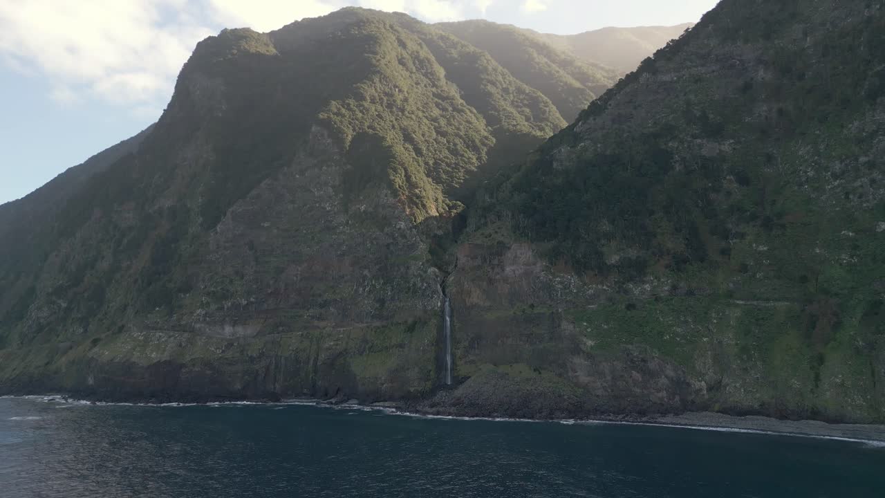 imágenes de drones capturan la cascada véu da noiva en madeira, bañada en la luz del sol en medio de majestuosas montañas, con vistas panorámicas sobre el mar