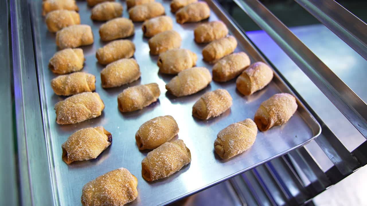 Metal baking sheet filled with freshly baked little croissants. Close up. Sweet desserts production at modern bakery.