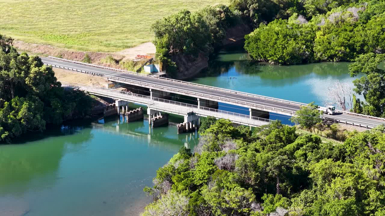 Aerial view of truck driving across bridge above lush river, bright daylight, steady camera movement