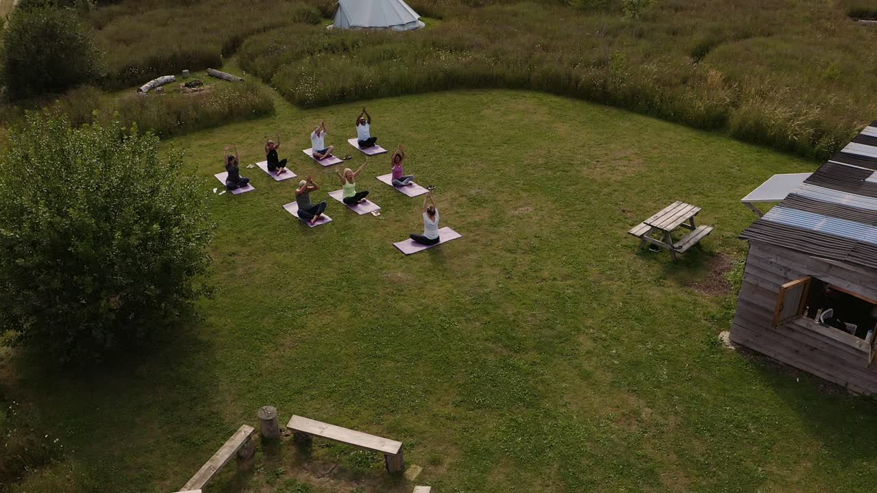 tomada con avión no tripulado del maestro que lidera un grupo de hombres y mujeres maduros en clase en un retiro de yoga al aire libre