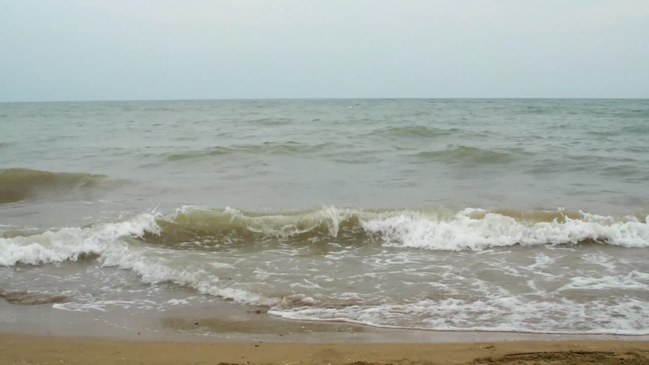 Small waves comes in on a sandy beach and the weather is not so fine.