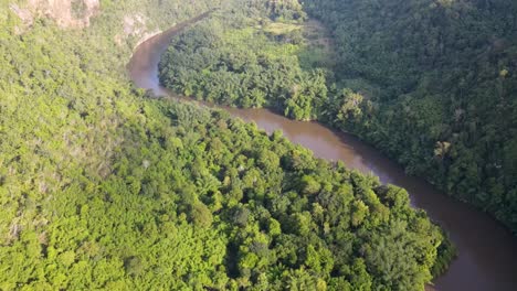 Spectacular-drone-view-of-River-Kwai-winding-through-jungle-leading-to-outstanding-mountain-views-in-the-background-in-Kanchanaburi,-Thailand