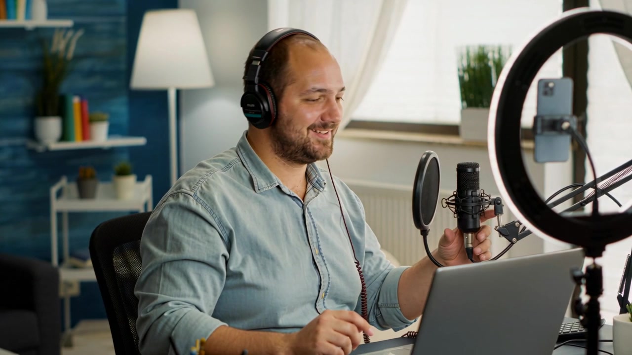 Uomo in camicia azzurra che indossa le cuffie e regola il microfono, avviando la registrazione di uno streaming nel suo ufficio domestico.