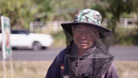 a man in beekeeping protective gear smiles outdoors