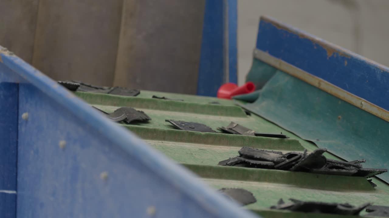 Shredded and crushed plastic fragments moving on green conveyor belt in plastic recycling facility