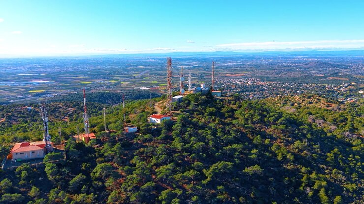 Torri di segnalazione si ergono su una collina in Spagna. Torri per le comunicazioni si innalzano sopra gli alberi sulla cima di una collina in Spagna, con campi e montagne distanti in vista.