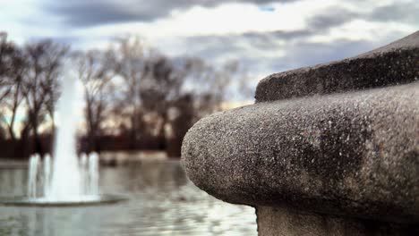 close-up footage of a unique concrete post in front of a scenic pond and flowing fountain at an outdoor park