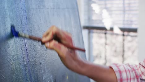 Hand-of-biracial-female-artist-painting-on-canvas-in-art-studio,-slow-motion