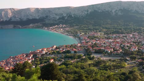 los frondosos árboles verdes junto a las montañas que dominan la pintoresca ciudad de baska y el tranquilo mar azul en krk, isla, croacia