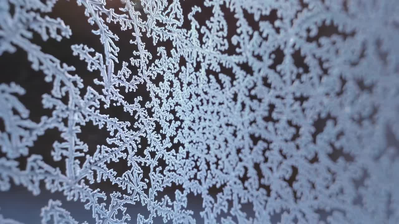 Close-up video of intricate frost patterns on glass, captured at an oblique angle