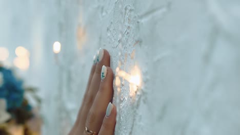 girl-touches-the-wall-with-a-hand-among-small-lamps-close-up