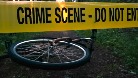 low angle of fallen bicycle behind the crime scene tape, accident scene. bike wheel spinning lying on the ground on summer evening forest trail. incident site on wooded area road. true crime setting