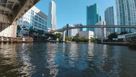 view-from-a-small-watercraft-as-it-passes-beneath-bridges-toward-the-tall-building-in-the-city-of-Miami-Florida-on-a-sunny-day-with-blue-skies