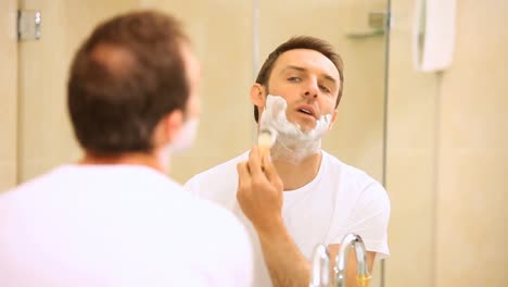 handsome man shaving his beard in front of a mirror