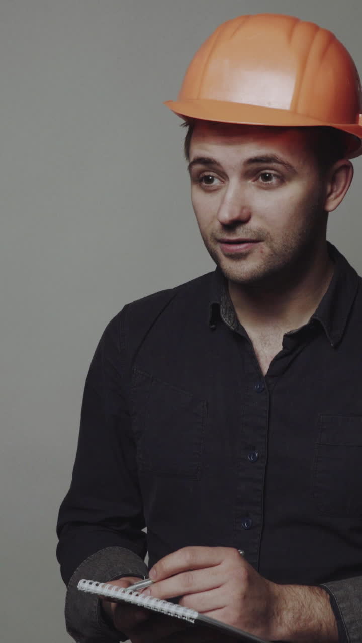 Young man architect in building helmet. Smiling young man architect in building helmet standing and writing on clipboard