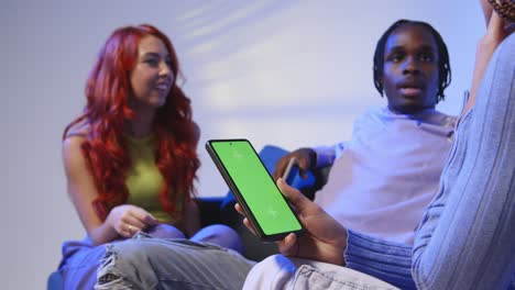 Close-Up-Of-Woman-With-Green-Screen-Mobile-Phone-Sitting-With-Gen-Z-Friends-Talking-And-Sharing-Posts-3