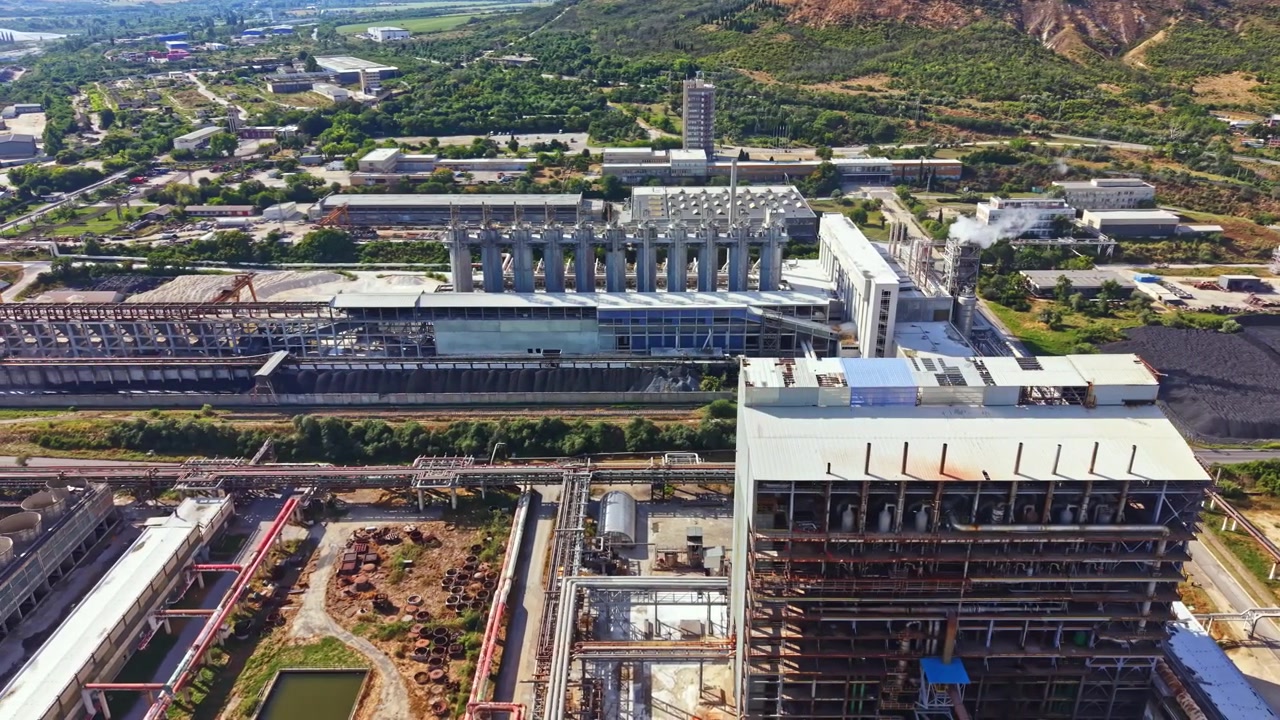 Industrial complex located in a mountainous region with multiple buildings, machinery, and green areas visible in the background during daytime hours
