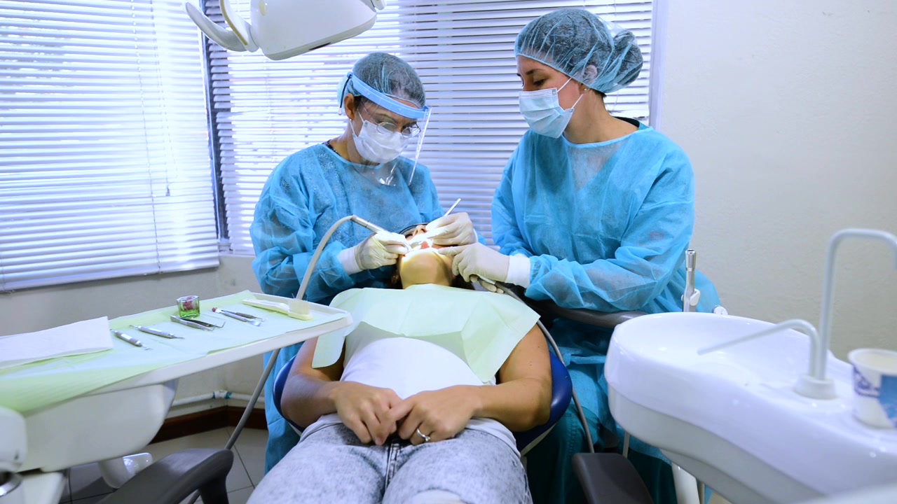 Dois dentistas profissionais trabalhando na boca de uma jovem mulher.