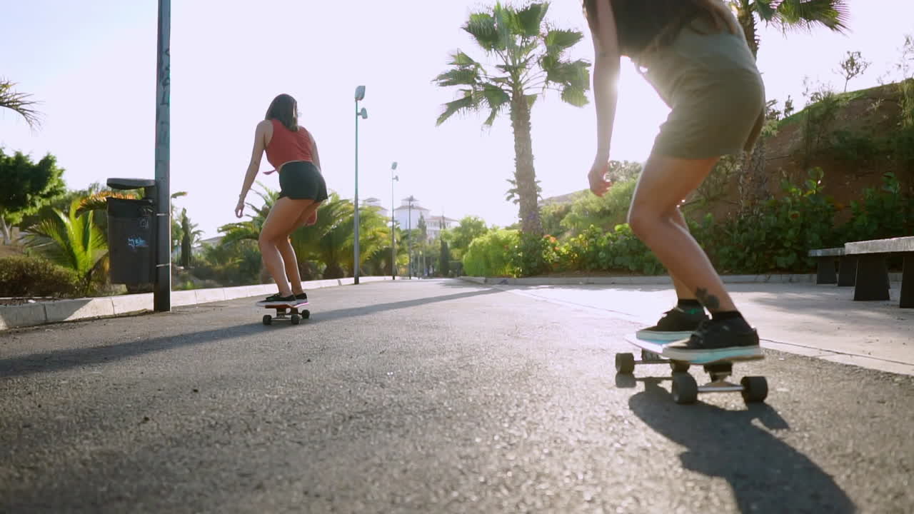 bajo la puesta de sol, dos jóvenes mujeres hispanas patinando en una isla, su viaje documentado en cámara lenta a lo largo de los caminos del parque. celebrando la felicidad y el bienestar