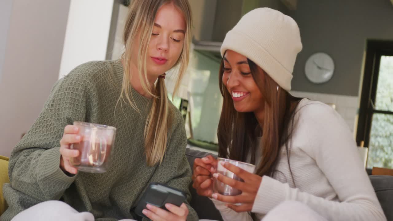 felices adolescentes diversas amigas bebiendo café y usando el teléfono inteligente en casa, cámara lenta