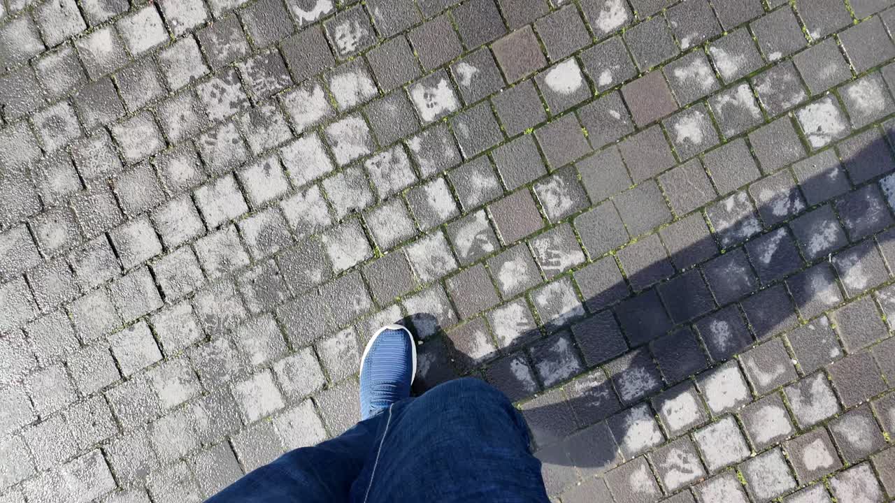 Person walking on a cobblestone pavement from a top-down view