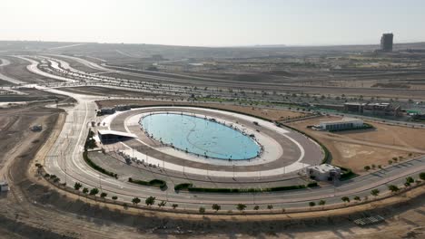 Toma-Panorámica-Aérea-De-Una-Fuente-De-Agua-Ovalada-Al-Lado-De-Una-Carretera-En-La-Ciudad-De-Bahria-En-Karachi,-Pakistán