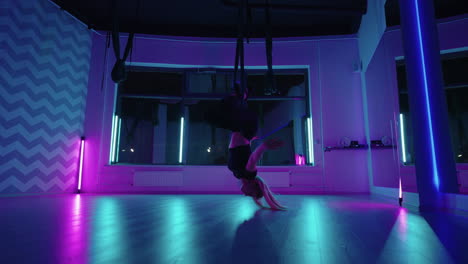 una mujer hace yoga y se estira en una hamaca colgante a la luz del neón. una chica joven y delgada practicando yoga con mosca en el gimnasio.