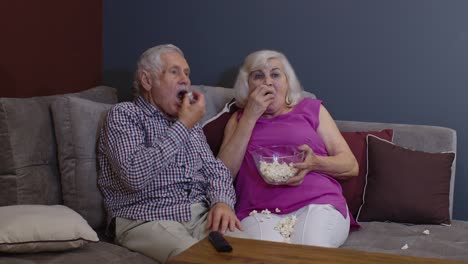una pareja de mayores viendo la televisión juntos en el sofá con palomitas de maíz