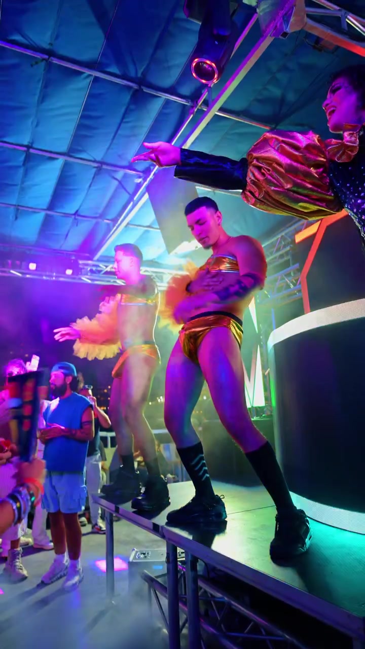 New York, USA, 7 juni 2026: Dragartist och muskulös dansare uppträder på ett prideevenemang. En dragqueen och en man i guldtrosor står på en scen med en ljus LED-skärm i bakgrunden.