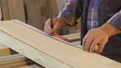 senior carpenter measures wood by meter in workshop.