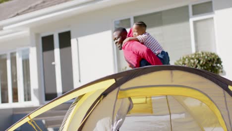 Glücklicher-Afroamerikanischer-Vater-Und-Sohn,-Die-Huckepack-Spielen-Und-Im-Sonnigen-Garten-Campen,-In-Zeitlupe