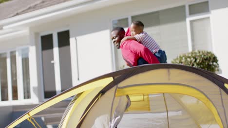 padre e hijo afroamericanos felices jugando a caballo y acampando en un jardín soleado, en cámara lenta