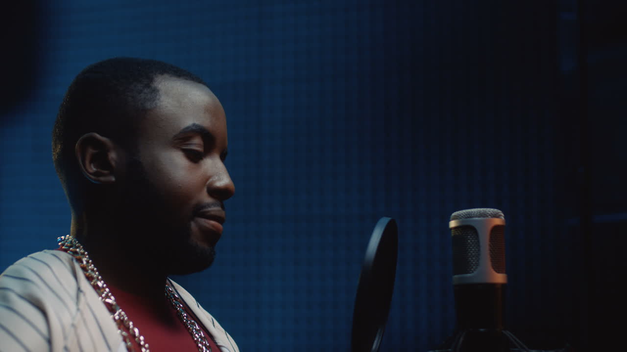 헤드폰을 끼고 어두운 사운드 스튜디오에서 노래를 녹음하기 시작하는 모자를 쓴 청년