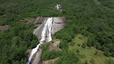 Approaching-wide-stream-of-clean-glacier-water-running-down-slippery-rock-at-lush-mountainside-Loen-Norway--Aerial-approaching-waterfall-and-looking-upwards---River-ending-in-Lovatnet-lake