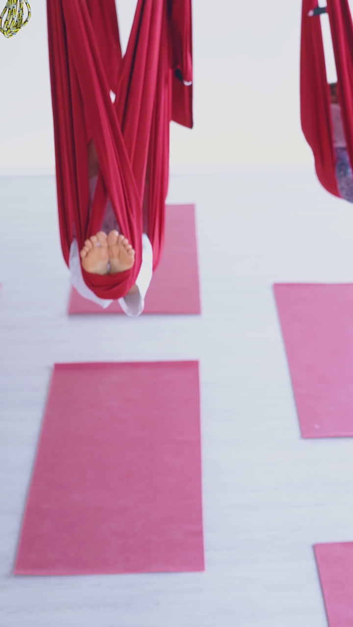 relaxed ladies group with bare feet sleeps swinging in red aerial fly yoga hammocks above fitness sport mats
