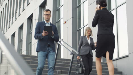 busineswomen and businessman walking up and down steps in the street near to office building