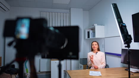 female speaker sitting at desk talks to camera. professional footage of blog content in studio.