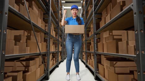 full body of asian female courier in blue uniform celebrating succeed delivering a carton in warehouse