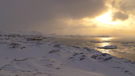 wide slow motion pan of the coastal city of llulissat in greenland at sunset with icebergs and glaciers in the background