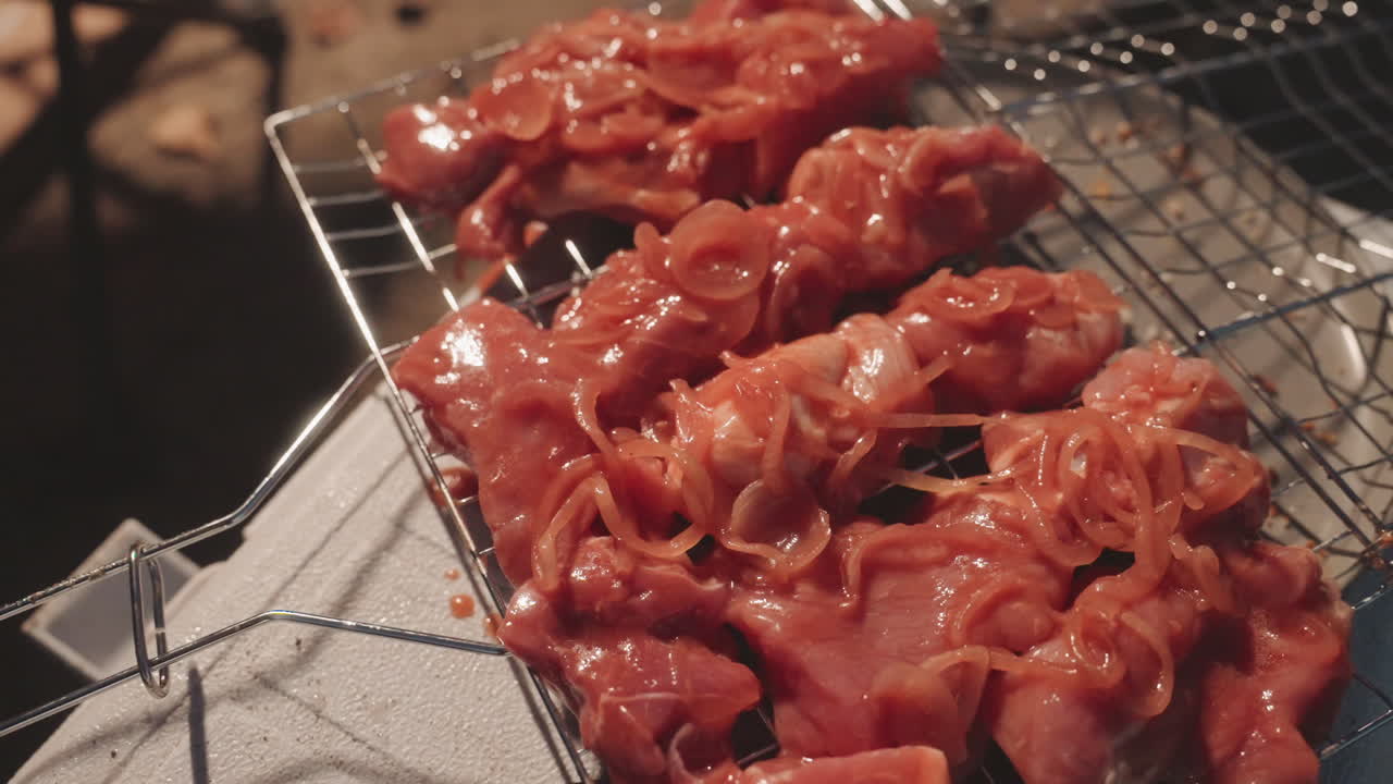 Spiedini marinati in primo piano sulla griglia che mostrano carne rossa lucida e superficie strutturata, succhi sfrigolanti che gocciolano sulla griglia a rete, cuoco da campo che prepara spiedini con le pinze, bagliore fumoso dalle braci, cibo intimo