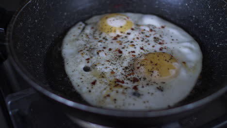 huevos fritos espolvoreados con pimienta y hojuelas de chile chisporroteando en una sartén