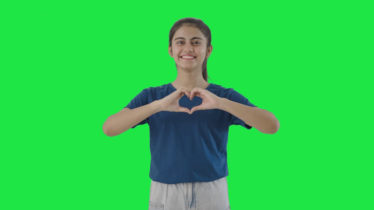 una adolescente india feliz haciendo un signo de corazón en la pantalla verde