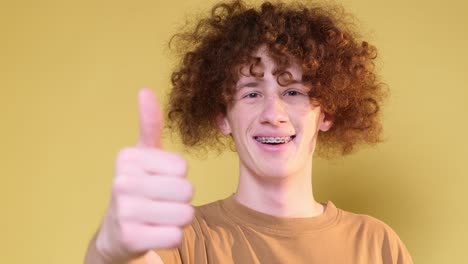 smiling curly young man on yellow background gesturing with hands he raises thumb up smiling curly young man on yellow background gesturing with hands he raises thumb up