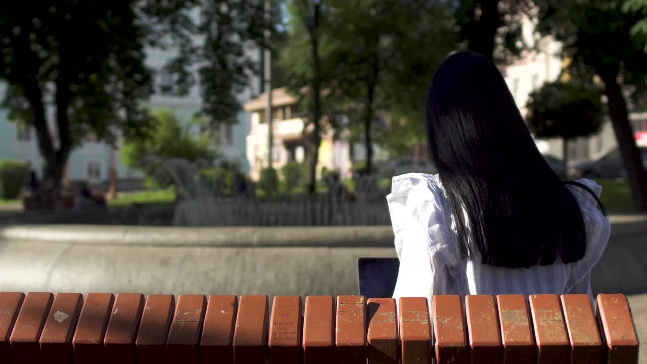 Young brunette with long hair working at laptop in park