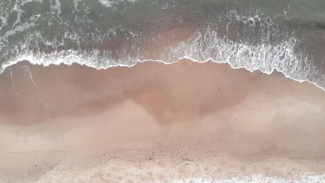 Aerial-shot-of-waves-crashing-into-sandy-beach-of-Ustka-in-winter