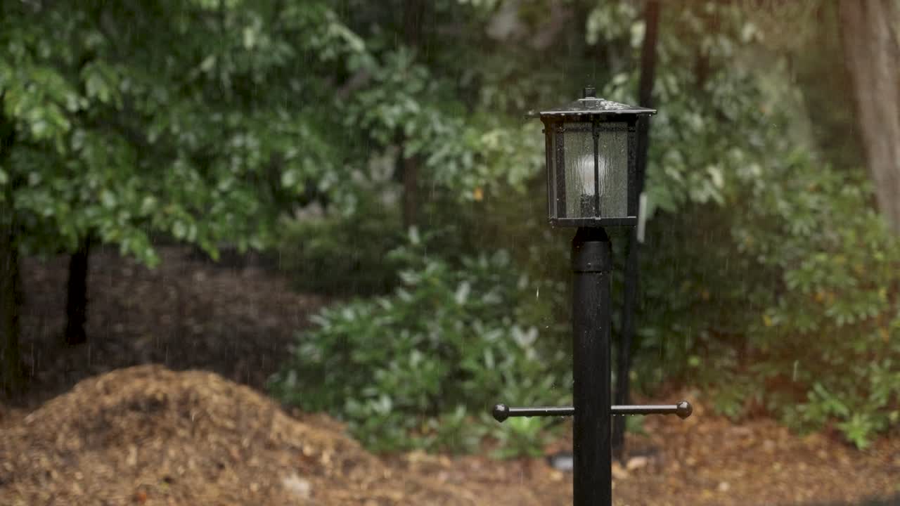 Shaky look at rain falling on a driveway lamp post.