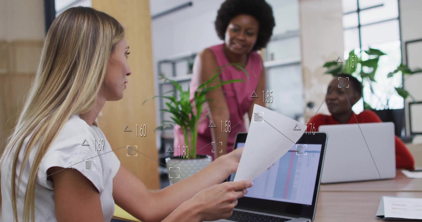 Women collaborating in office with data processing animation over laptop screen