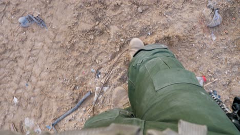 clip of soldiers feet as he walks along passing tyre tracks and assorted debris n